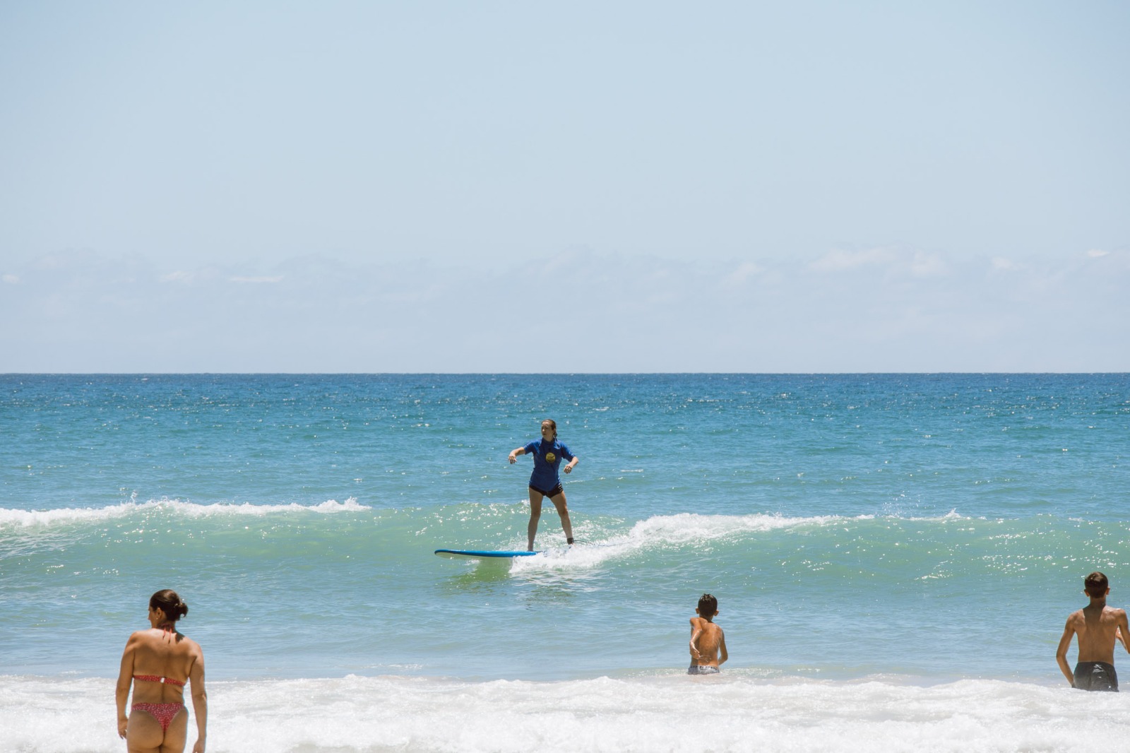 Aluna surfando entre banhistas